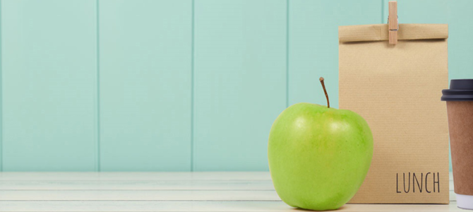 A brown lunch bag with a green apple and takeaway cup of coffee.