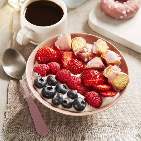 A bowl of yogurt filled with fruit and Fibre One™ 90 Calorie Strawberry & Cream Flavour Doughnut pieces with a container of agave nectar